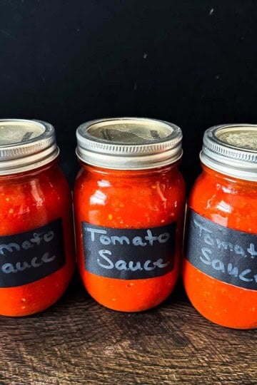 Three jars of homemade canned tomato sauce made with fresh tomatoes using water bath canning.