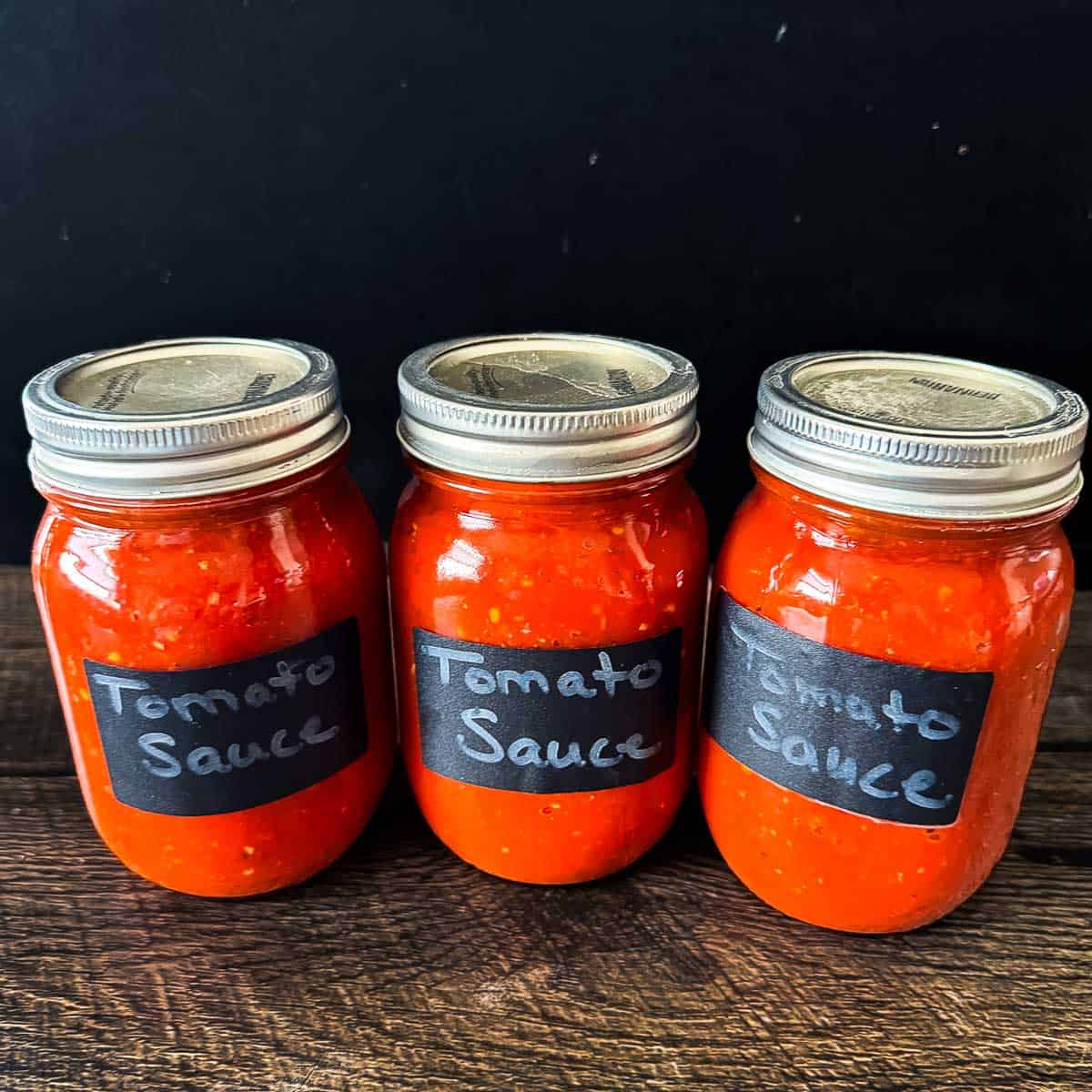 Three jars of homemade canned tomato sauce made with fresh tomatoes using water bath canning.