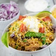Slow cooker chicken burrito bowl topped with grated cheese and sour cream.