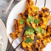 Chicken satay recipe on skewers on a white plate.