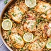 A skillet filled with Greek Lemon chicken and rice, garnished with fresh parsley and slices of lemon.