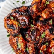 Grilled BBQ chicken thighs on a white serving plate.
