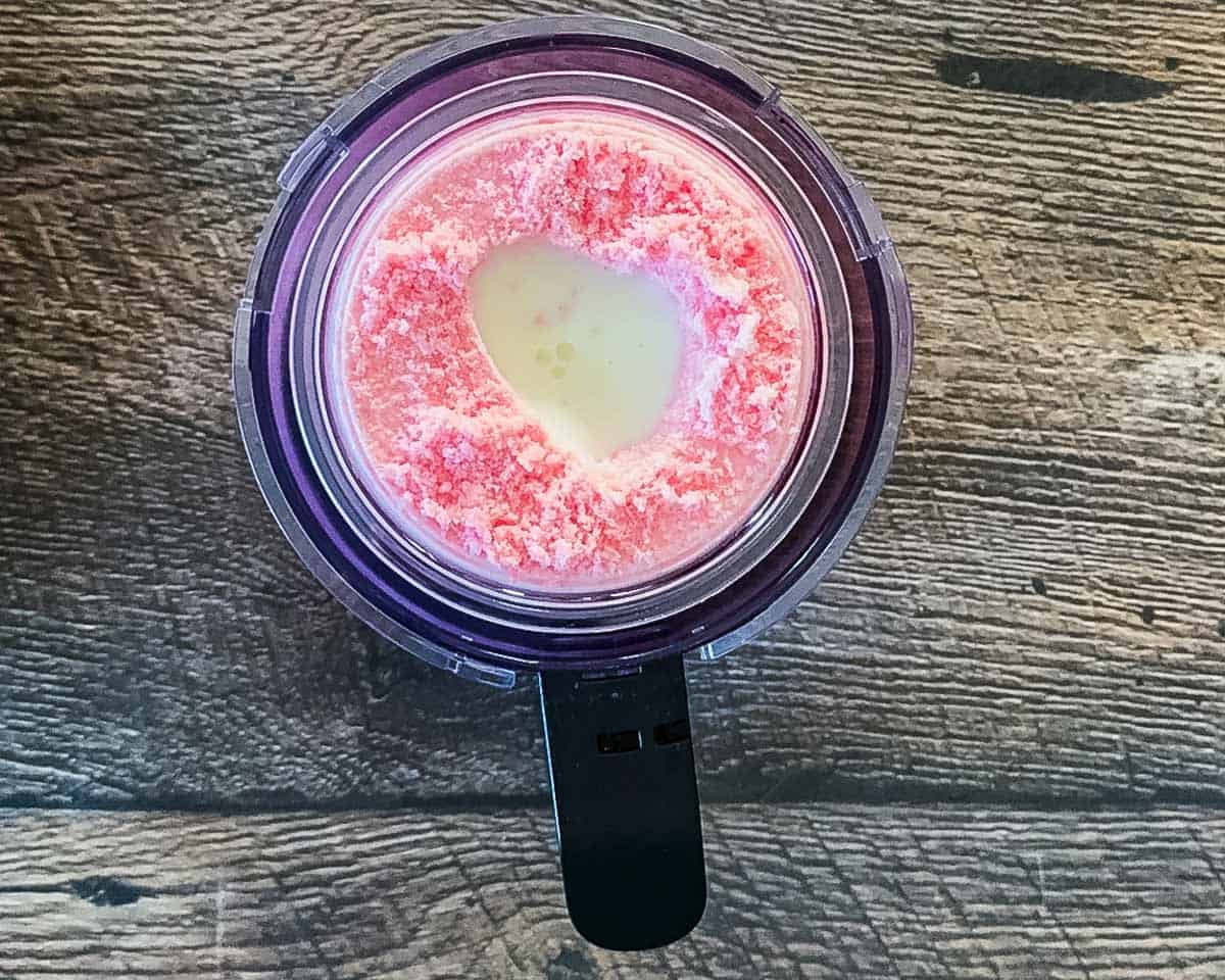 Looking down into a crumbly pint of strawberry ice cream with a small splash of liquid milk added to the center well, preparing it for a re-spin.