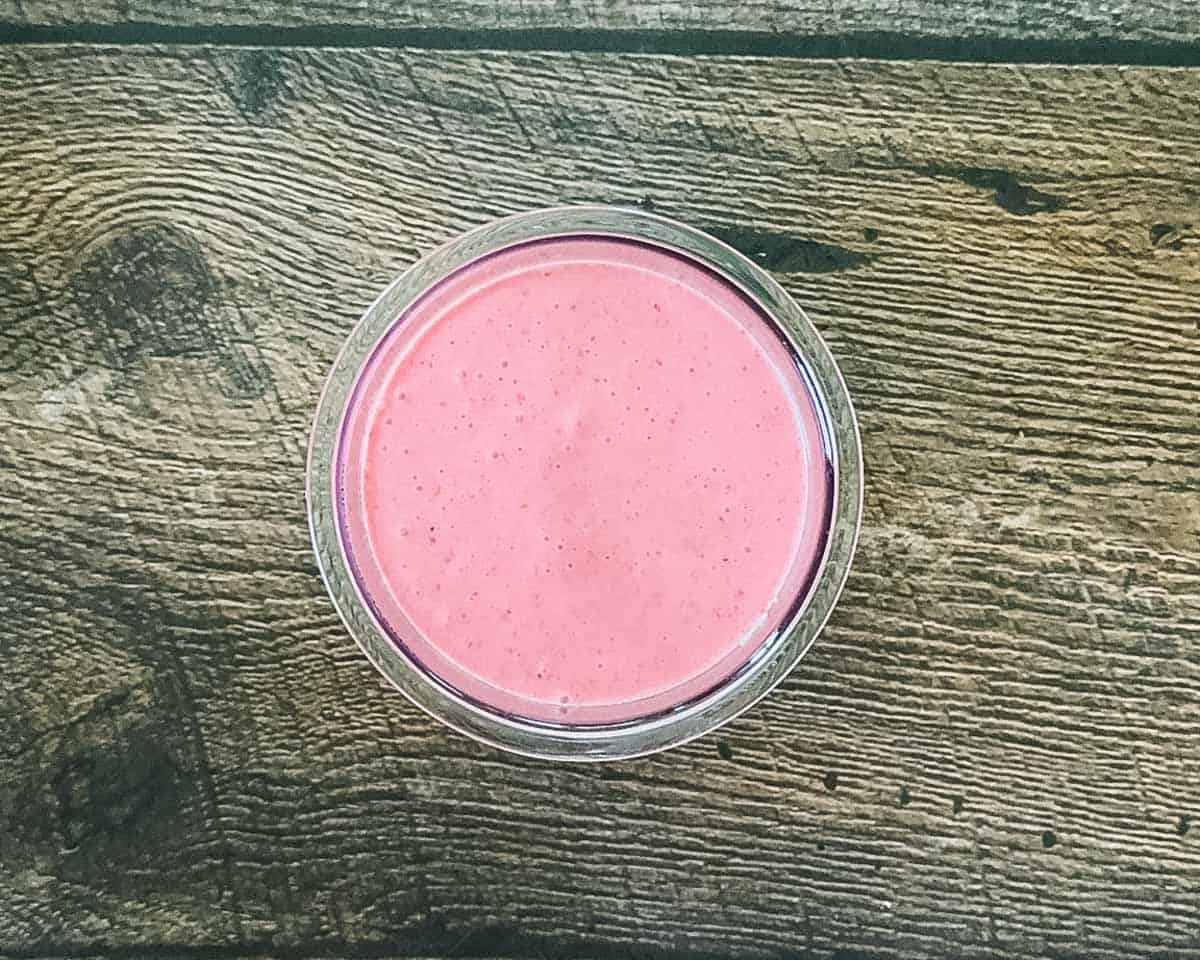 An overhead view of a Ninja Creami pint filled up to the max fill line with a smooth, bright pink blended strawberry liquid base before freezing.