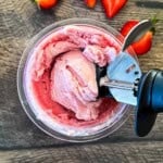 Close-up overhead view of a black ice cream scoop digging into a fresh pint of creamy strawberry ice cream made in the Ninja Creami.