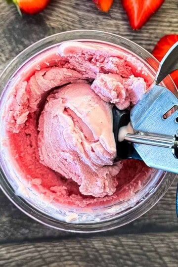 Close-up overhead view of a black ice cream scoop digging into a fresh pint of creamy strawberry ice cream made in the Ninja Creami.