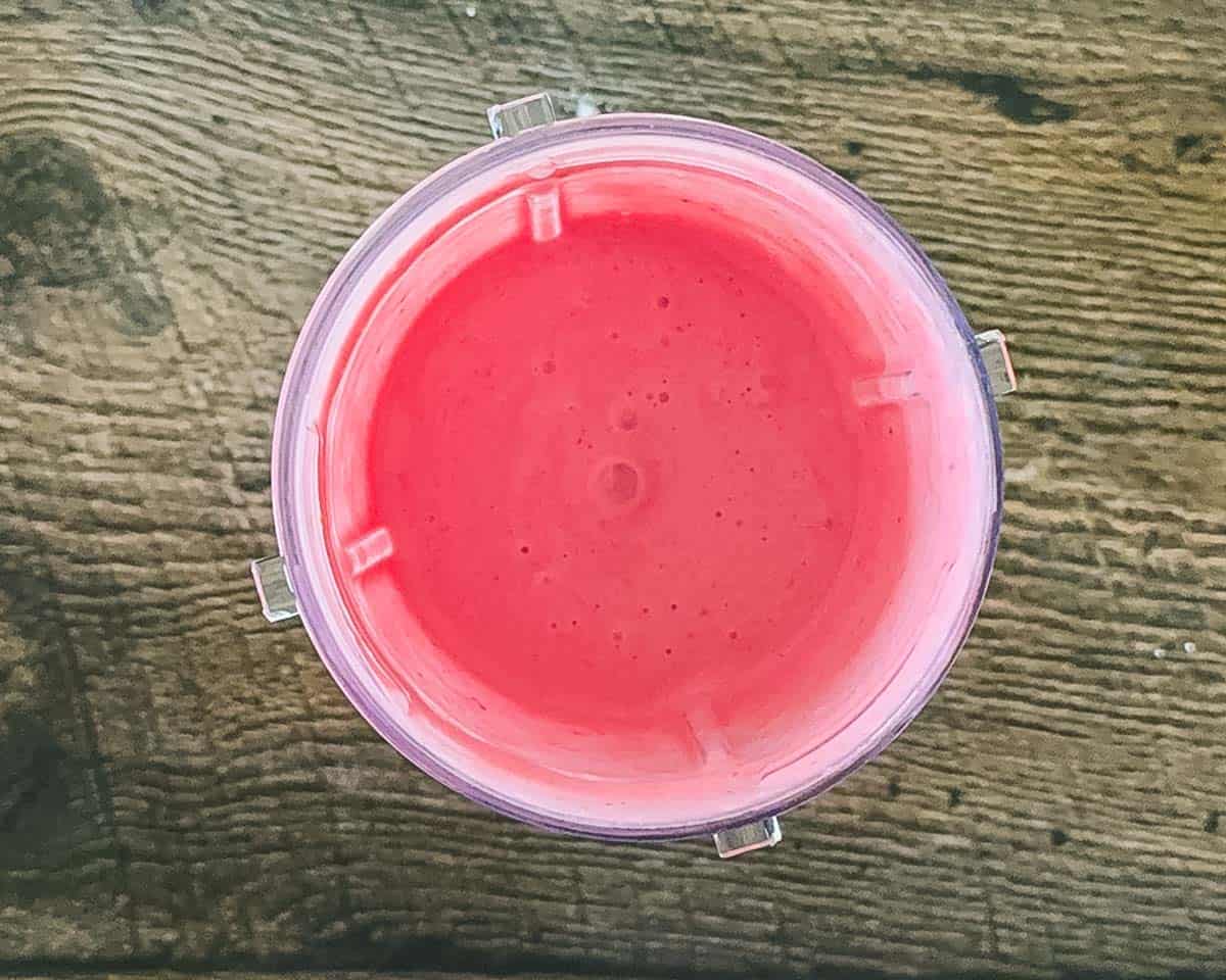 Looking down into a blender jar filled with the blended strawberry ice cream base.