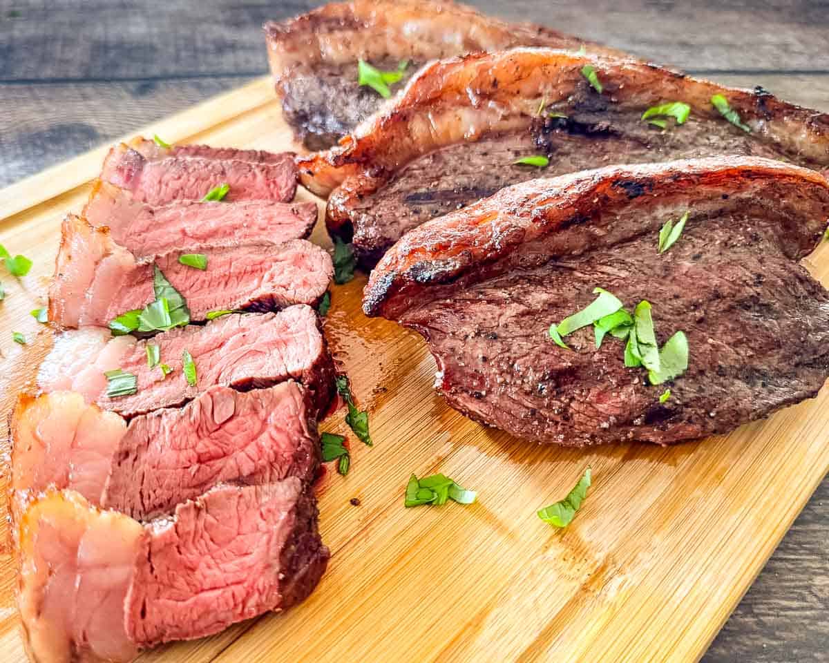 Pellet grill smoked picanha steak sliced and served on a cutting board with parsley.
