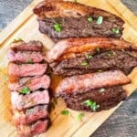 Smoked picanha steak sliced on a wooden cutting board, showing juicy medium-rare beef with a crispy fat cap and fresh parsley garnish.