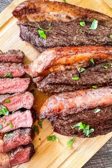 Smoked picanha steak sliced on a wooden cutting board, showing juicy medium-rare beef with a crispy fat cap and fresh parsley garnish.