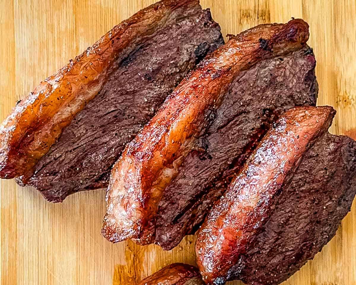 Cooked smoked picanha steaks with juicy beef and rendered fat caps on a cutting board.