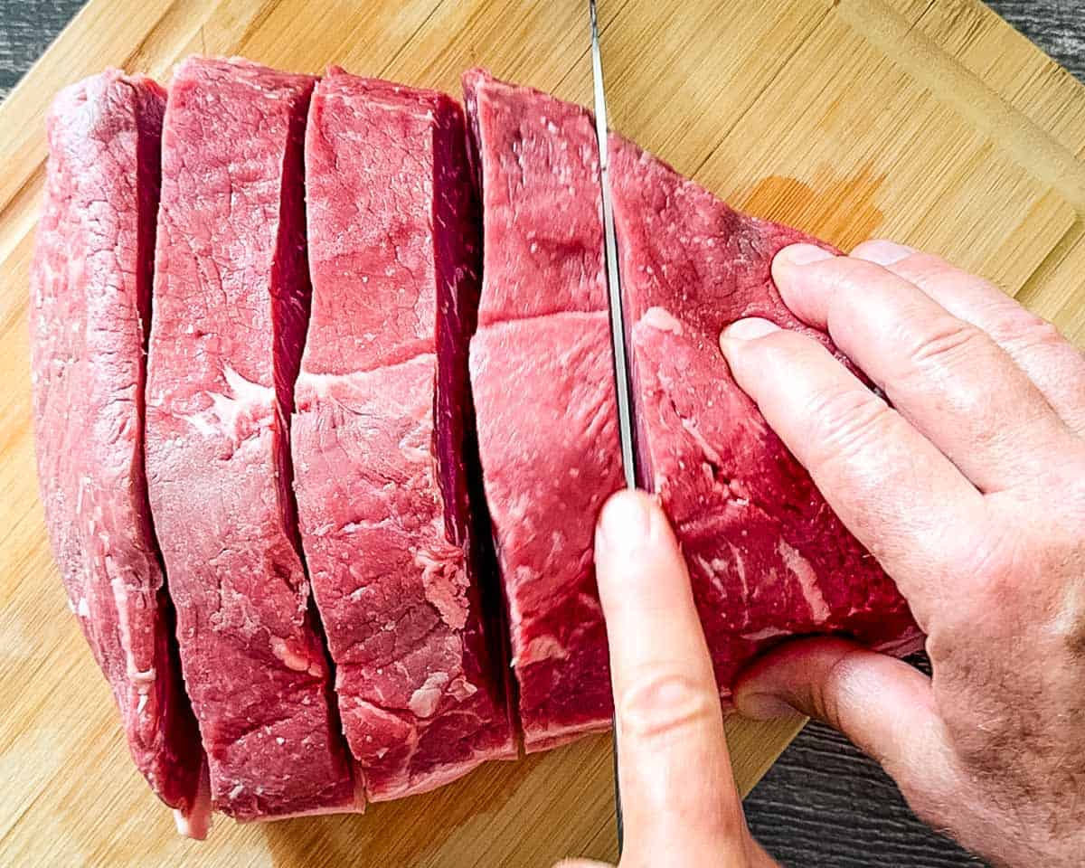 A sharp knife cutting the roast into thick steaks.