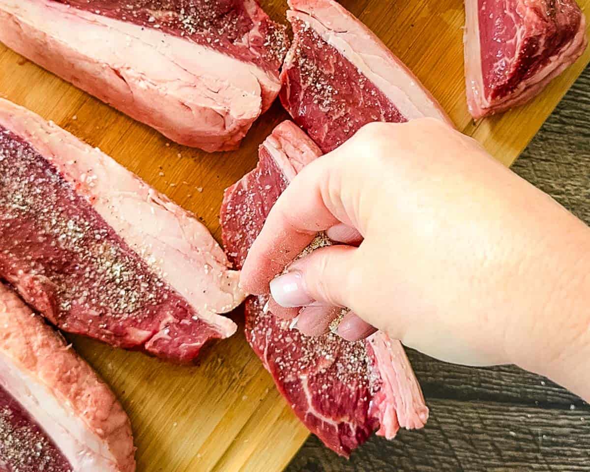 Seasoning raw picanha steaks before cooking on a pellet grill.