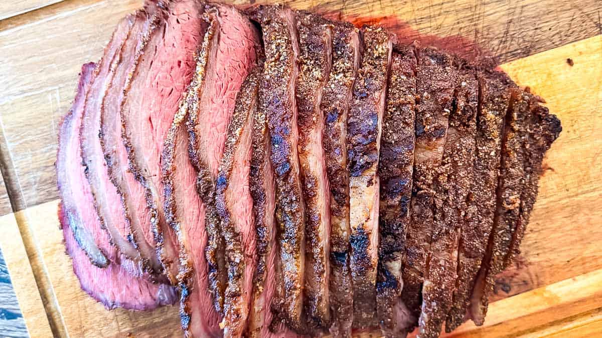 Smoked picanha roast sliced on a cutting board with a pink medium-rare center and rendered fat cap.
