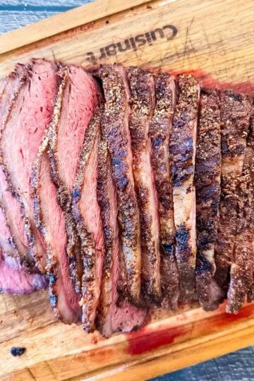Sliced smoked sirloin cap roast (picanha) on a wooden cutting board showing a juicy medium-rare center and crispy bark.