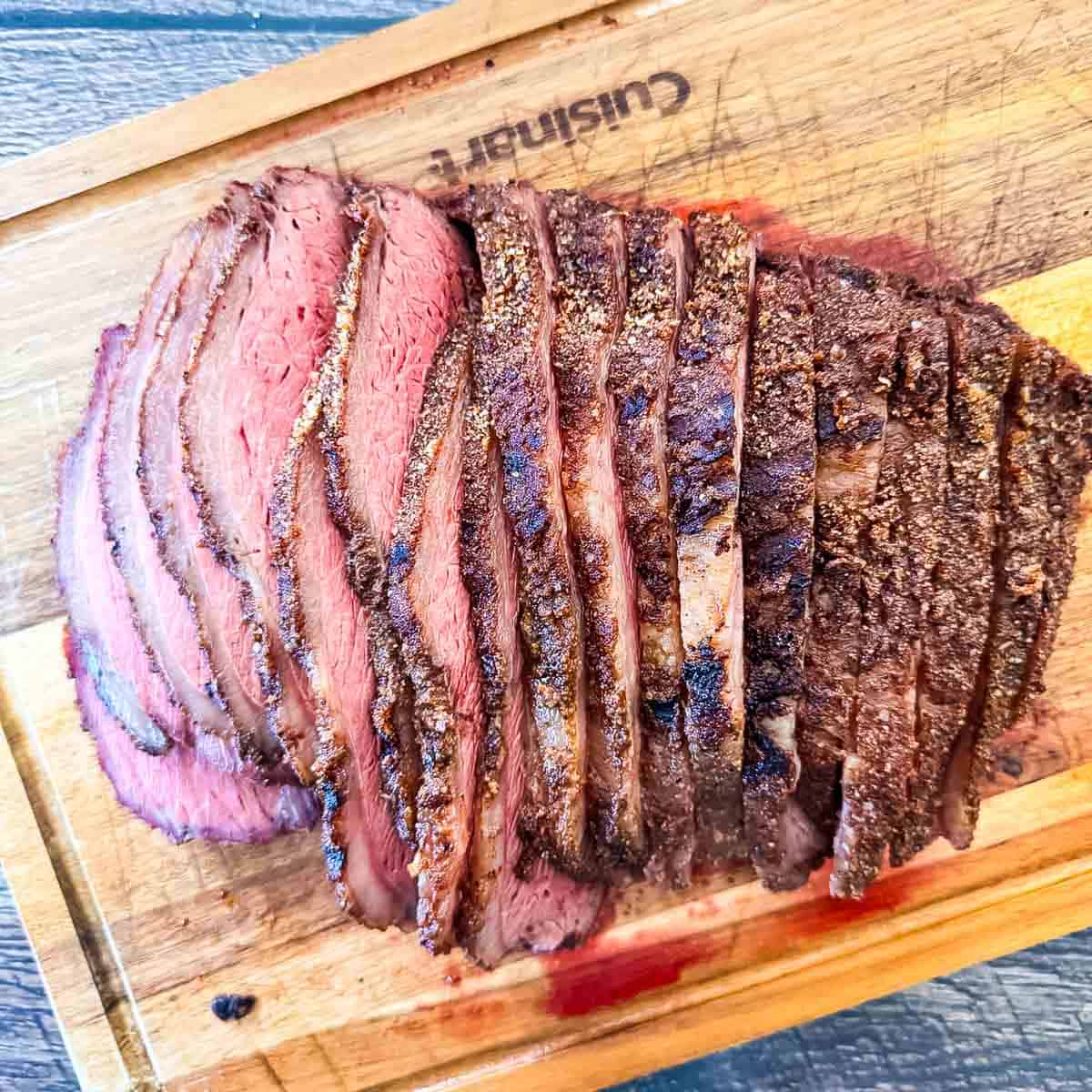 Sliced smoked sirloin cap roast (picanha) on a wooden cutting board showing a juicy medium-rare center and crispy bark.