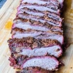 Smoked tri tip like brisket sliced on a cutting board with a smoky bark and pink smoke ring.