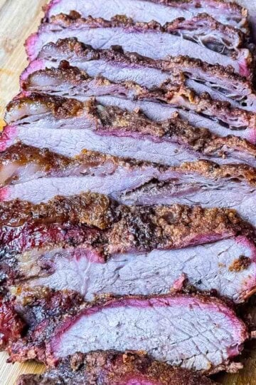 Smoked tri tip like brisket sliced on a cutting board with a smoky bark and pink smoke ring.