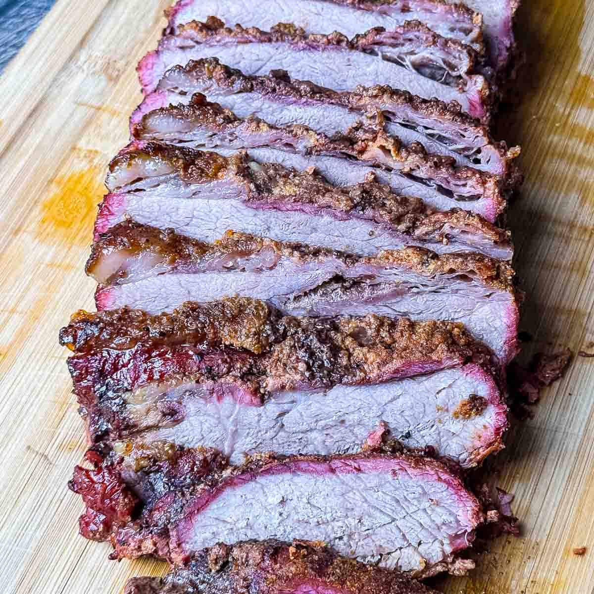 Smoked tri tip like brisket sliced on a cutting board with a smoky bark and pink smoke ring.