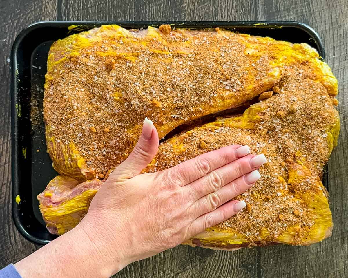 Pressing homemade brisket rub onto seasoned tri-tip roasts before smoking.