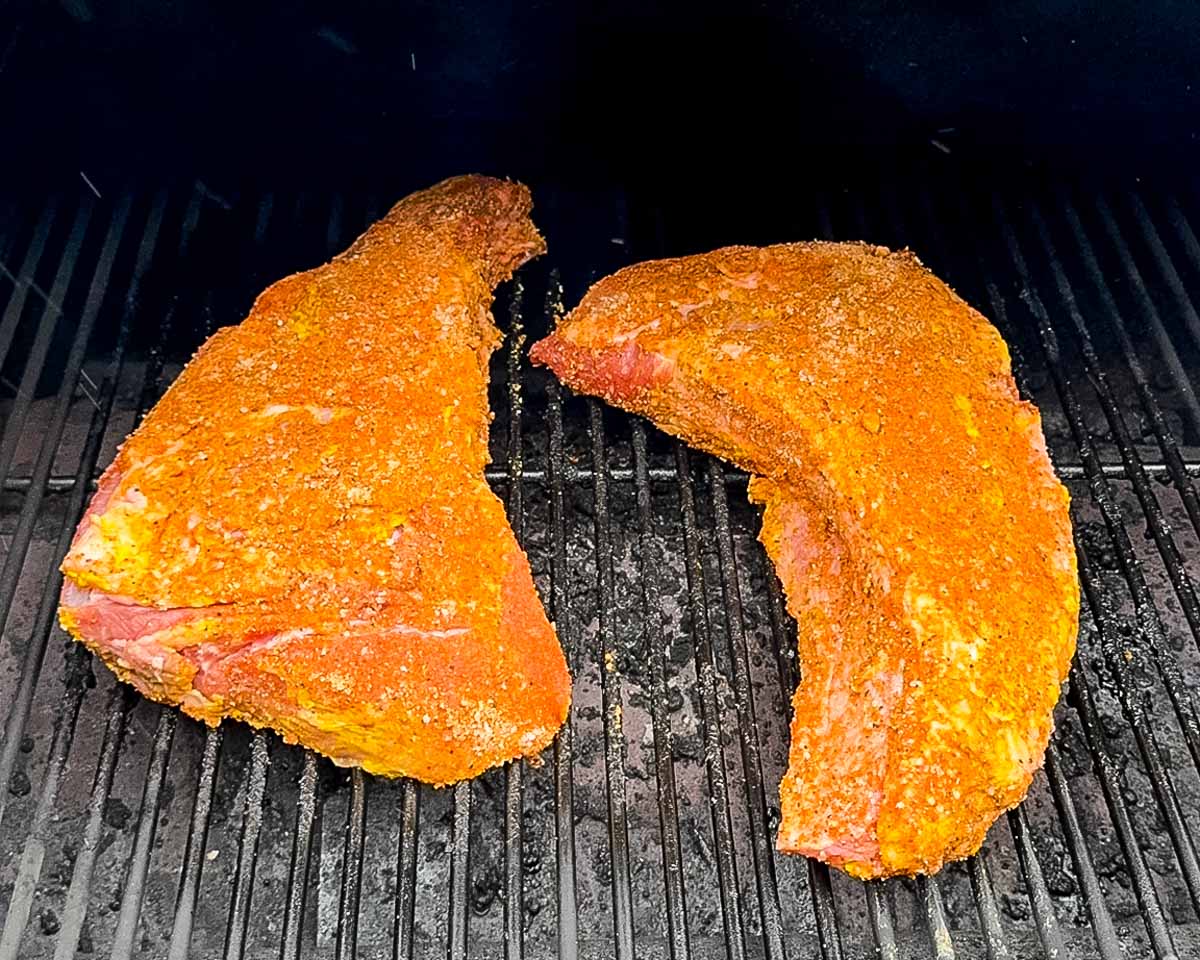 Two seasoned tri-tip roasts placed directly on the pellet grill grates before smoking.