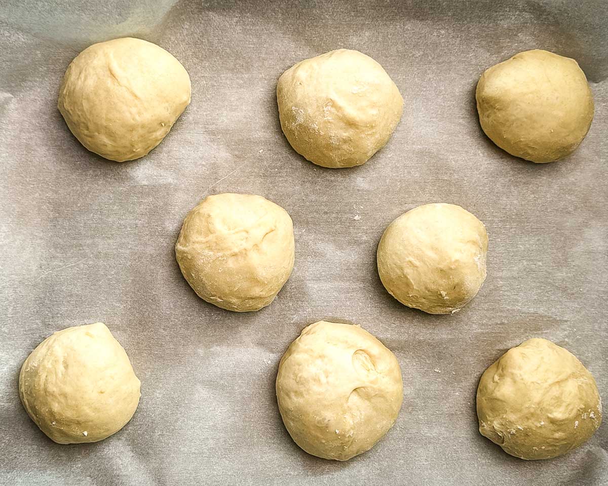 Sourdough bun dough divided and shaped into balls on a parchment-lined baking sheet.