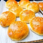 Soft and fluffy sourdough discard hamburger buns topped with sesame seeds cooling on parchment paper.