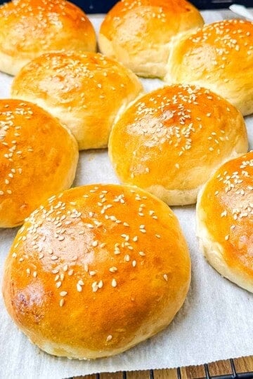 Soft and fluffy sourdough discard hamburger buns topped with sesame seeds cooling on parchment paper.