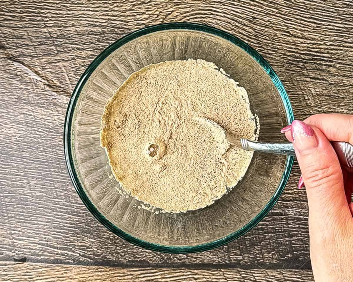Stirring active dry yeast and sugar into warm water for homemade hamburger buns.