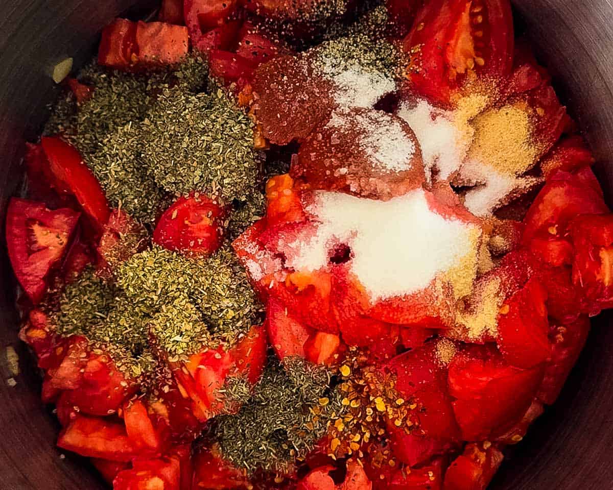 Chopped fresh tomatoes with dried herbs, garlic powder, onion powder, salt, pepper, and seasonings added to a large pot.