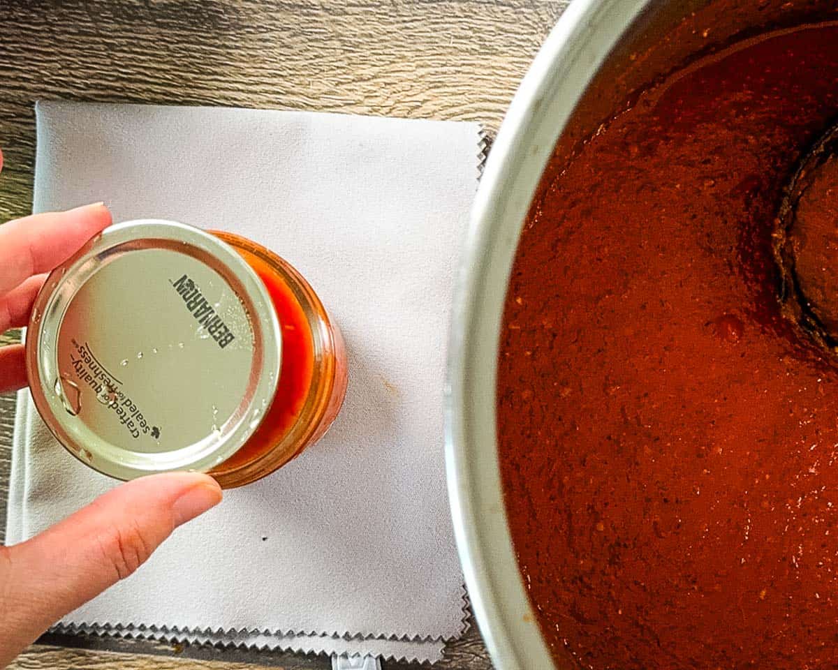 Fingers placing a lid on the jar filled with sauce.