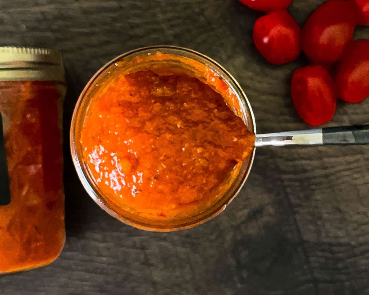 A spoon lifting up a scoop of pizza sauce from the jar, showing its thick texture.