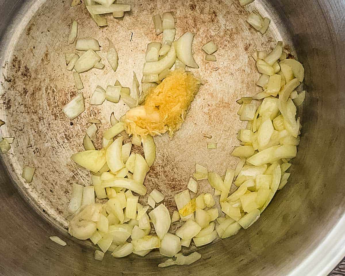 Chopped onion and garlic cooking in a large pot before adding tomatoes.