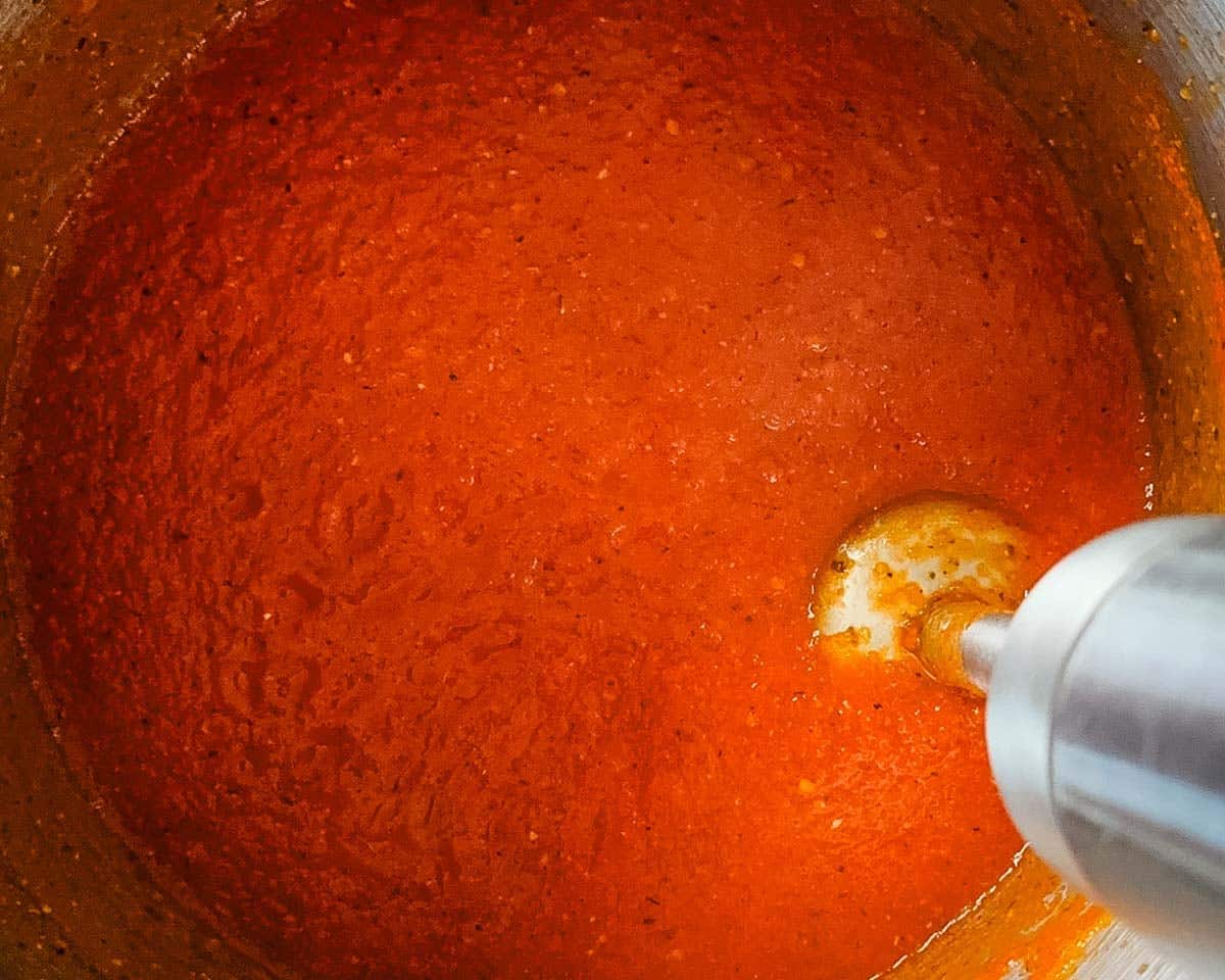 An immersion blender blending the sauce in a pot until smooth.