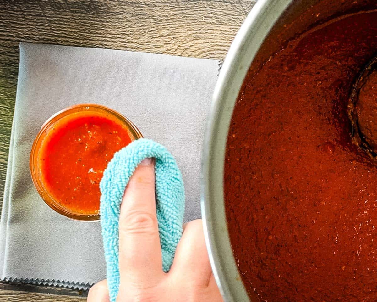 Wiping the rim of a mason jar with hot homemade pizza sauce before applying a lid.