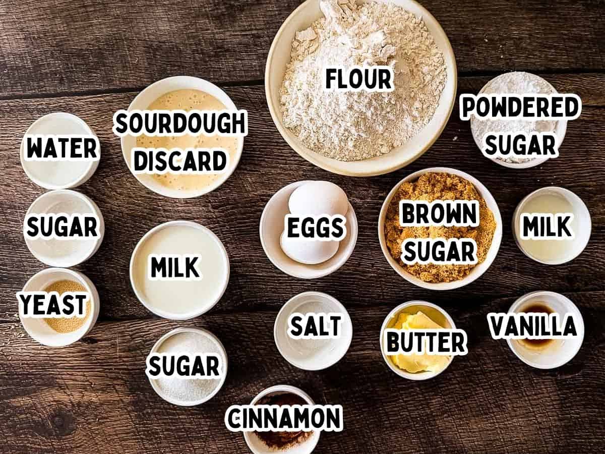 Labeled ingredients for sourdough discard cinnamon buns in white bowls placed on a wooden table.