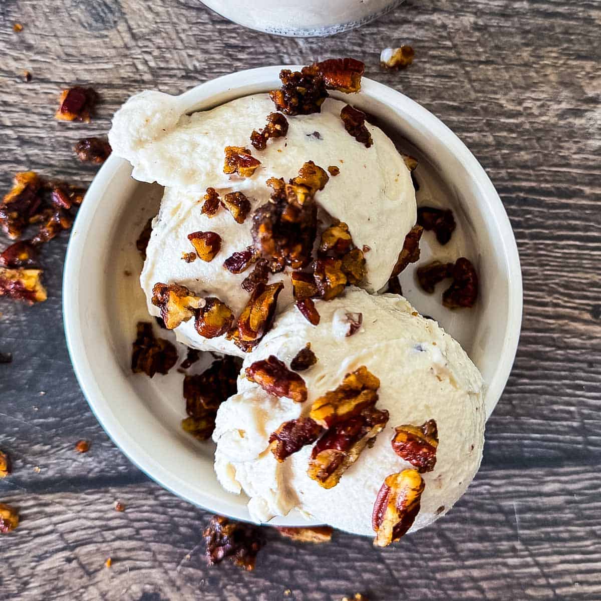 Scoops of butter pecan ice cream made in the Ninja Creami in a white bowl, topped with extra candied pecans.