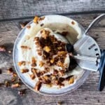 Ninja Creami butter pecan ice cream topped with candied pecans in a pint container with an ice cream scoop.