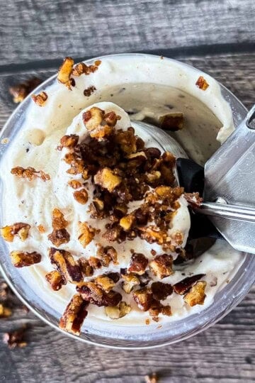 Ninja Creami butter pecan ice cream topped with candied pecans in a pint container with an ice cream scoop.