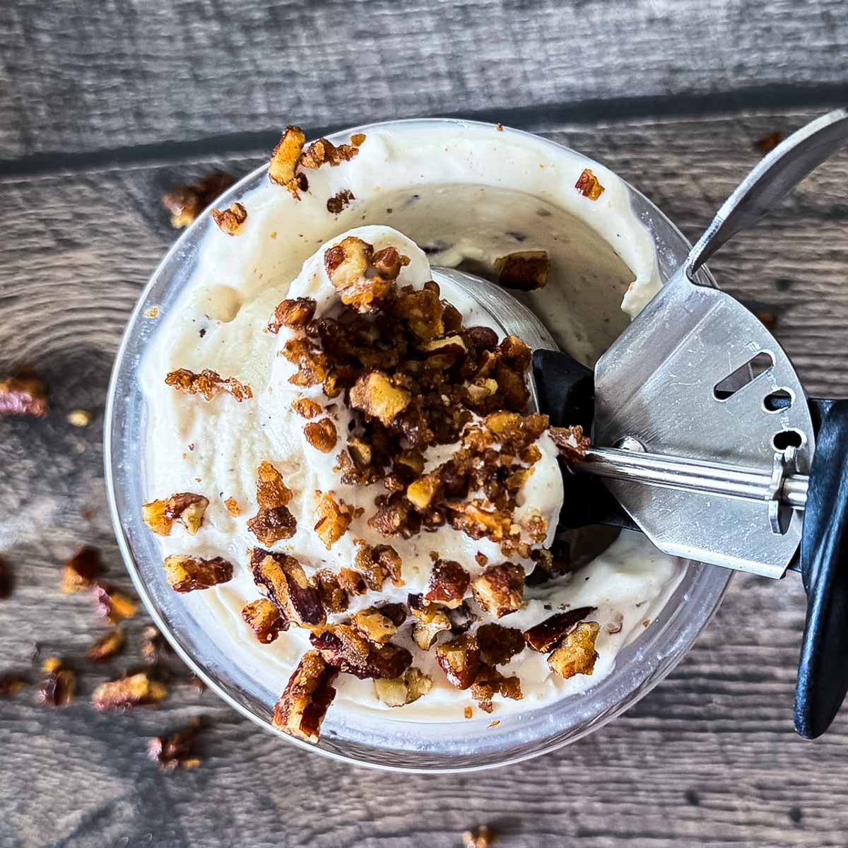 Ninja Creami butter pecan ice cream topped with candied pecans in a pint container with an ice cream scoop.