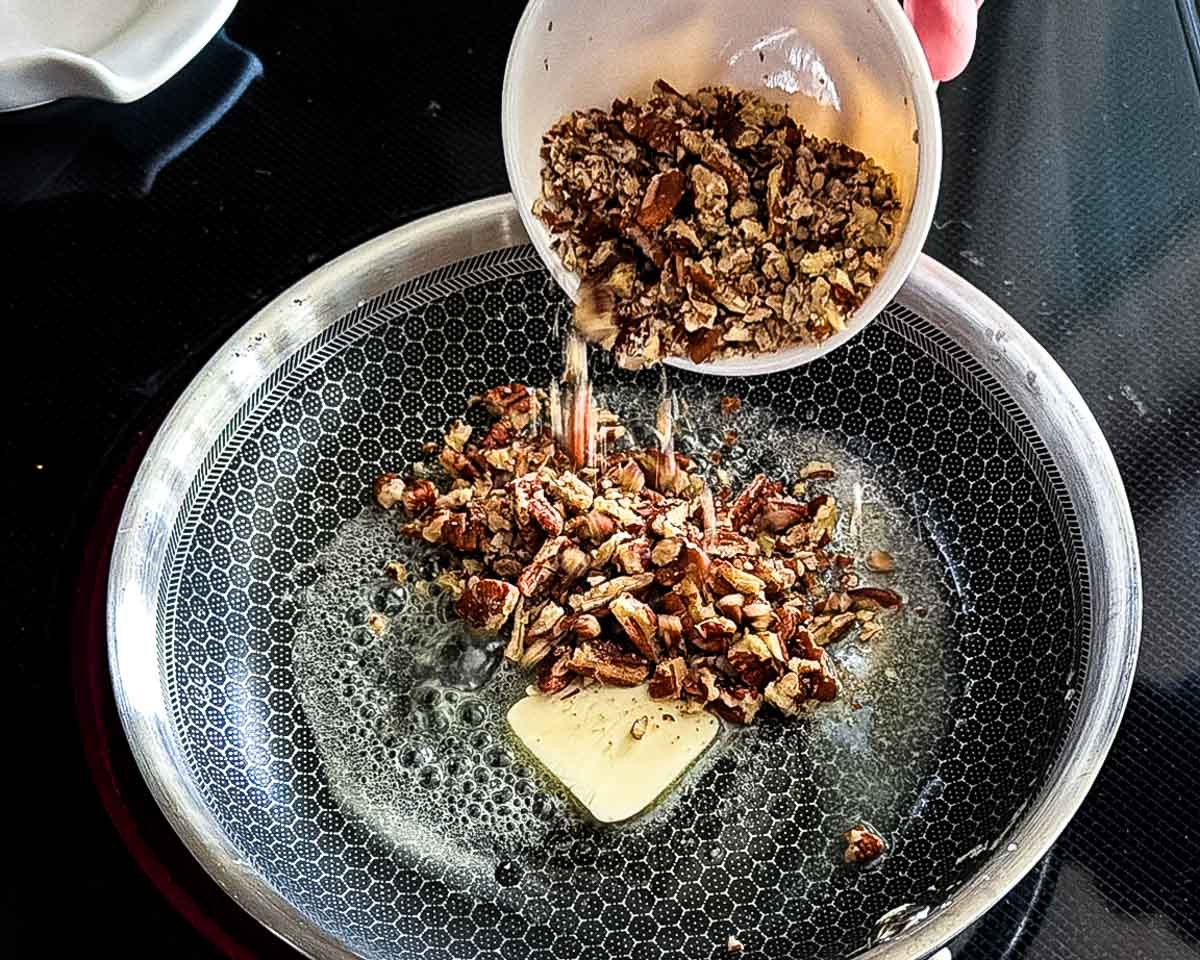 Chopped pecans being added in a skillet with melted butter.