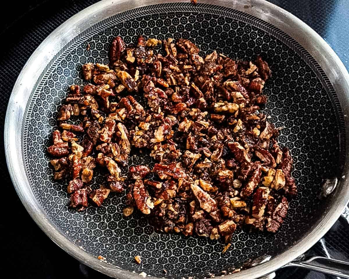 Candied pecans toasted in a skillet until browned and glossy.