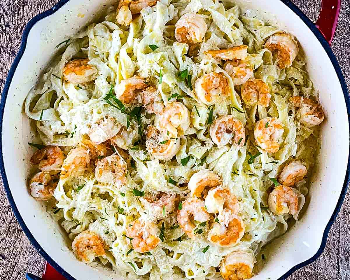 Finished Olive Garden shrimp Alfredo with creamy fettuccine, Parmesan cheese, and fresh parsley in a skillet.