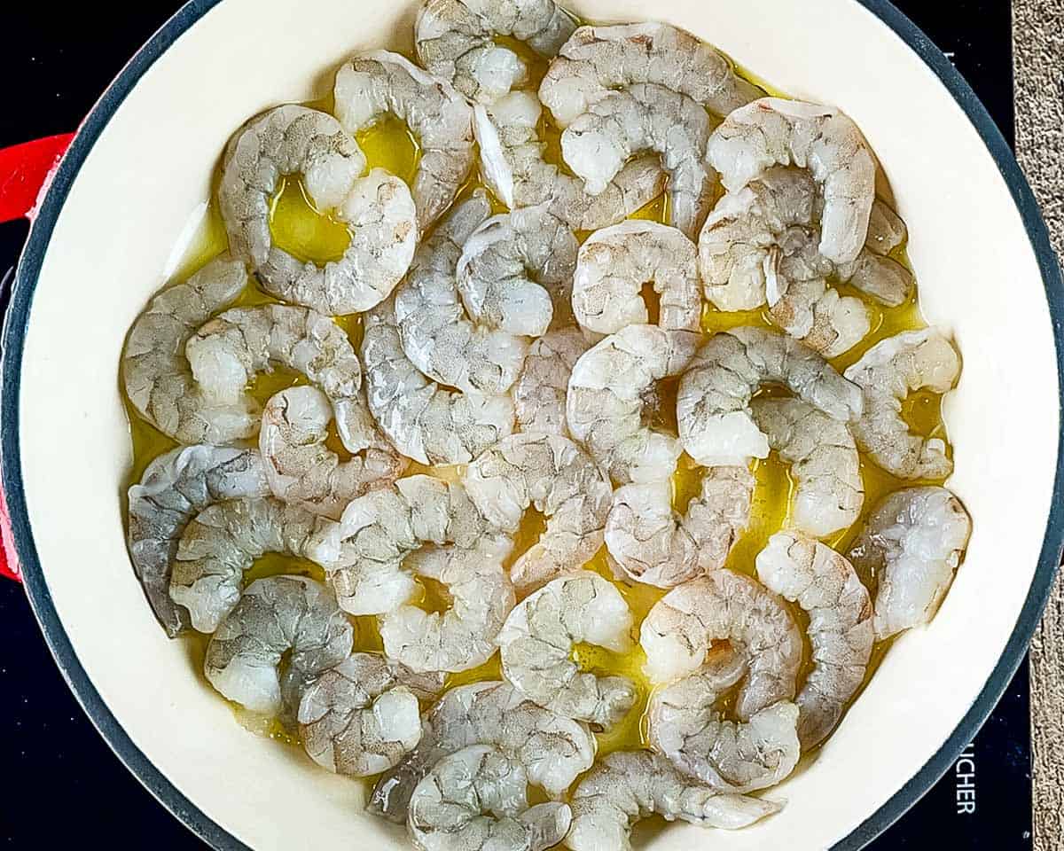 Raw peeled shrimp in a skillet with olive oil before seasoning and cooking.