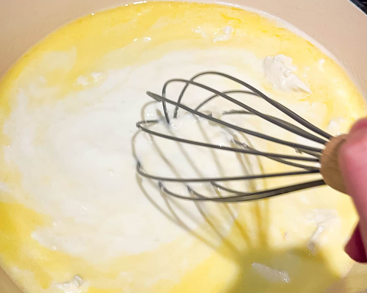 Whisking softened cream cheese into half and half and garlic butter for shrimp Alfredo sauce.