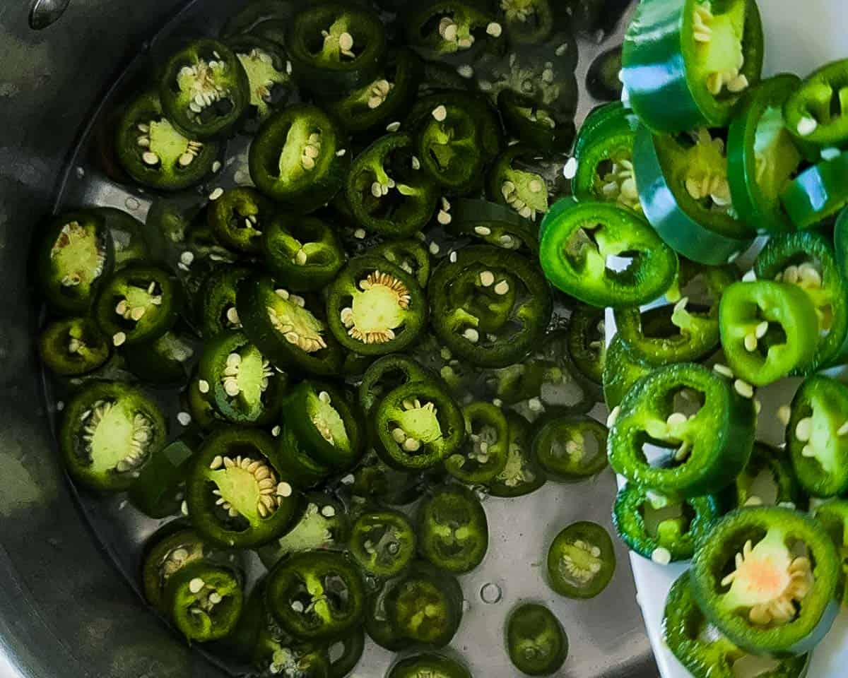 Fresh sliced jalapeño peppers being added to hot pickling brine in a saucepan.