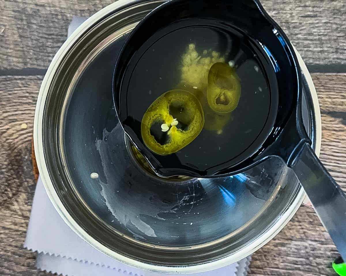 Ladling hot pickling brine over sliced jalapeño peppers in a mason jar.