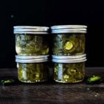 Homemade canned jalapeño peppers sliced into rings and packed in pickling brine in four small mason jars.