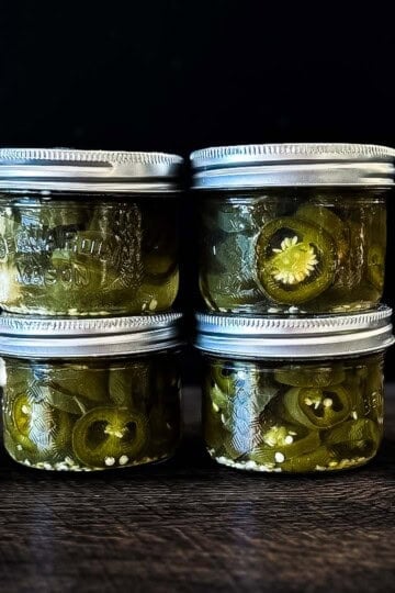 Homemade canned jalapeño peppers sliced into rings and packed in pickling brine in four small mason jars.