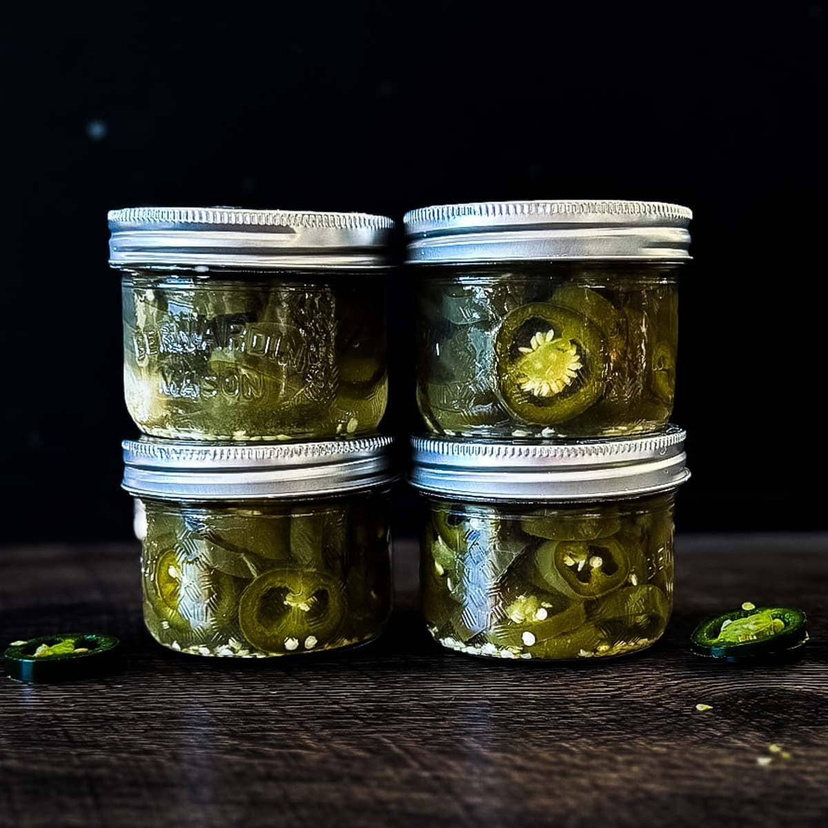 Homemade canned jalapeño peppers sliced into rings and packed in pickling brine in four small mason jars.